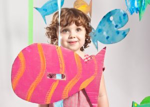 Child playing with colourfully painted cardboard fish cut outs